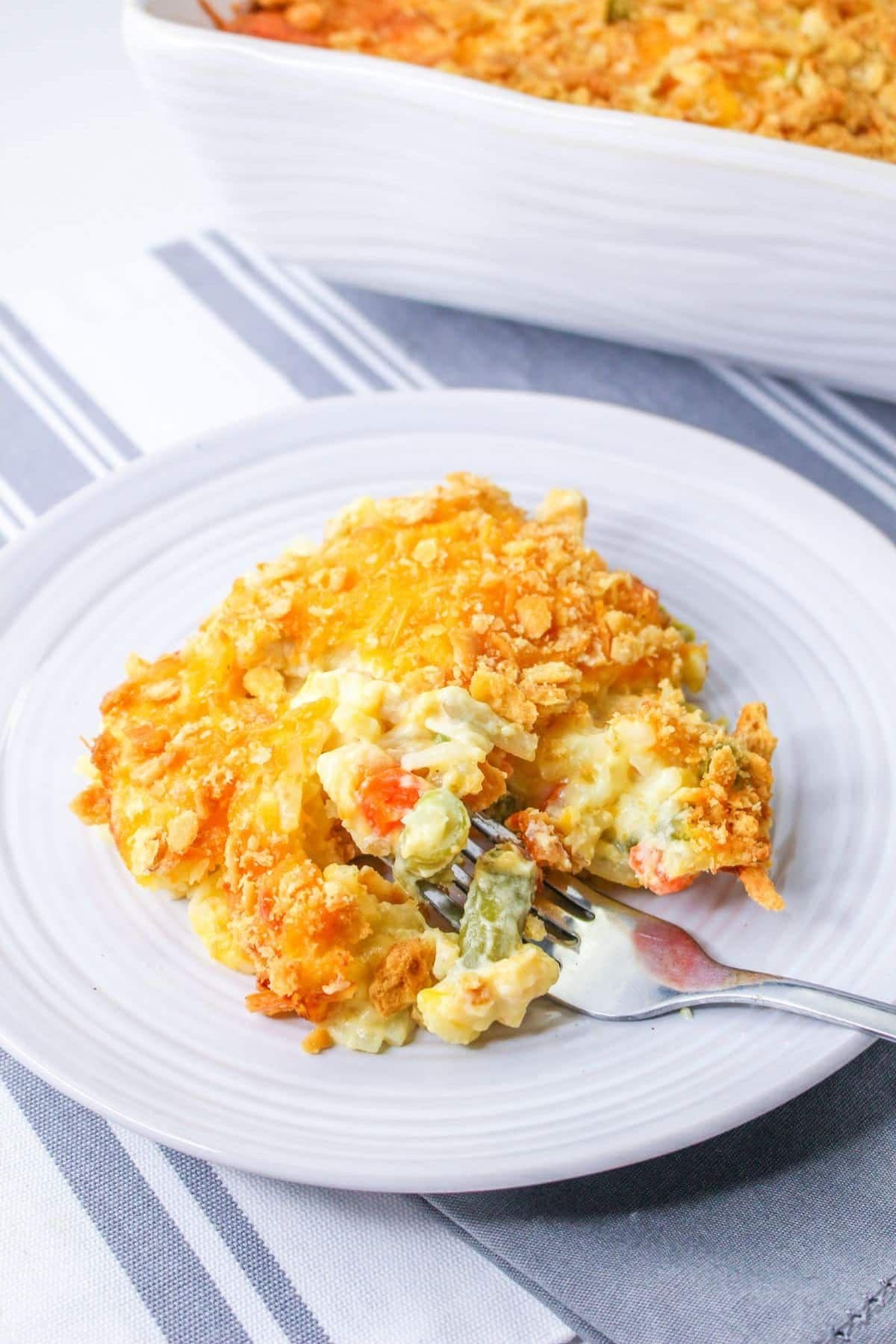 A serving of cheesy chicken casserole with crumb topping on a white plate and fork.