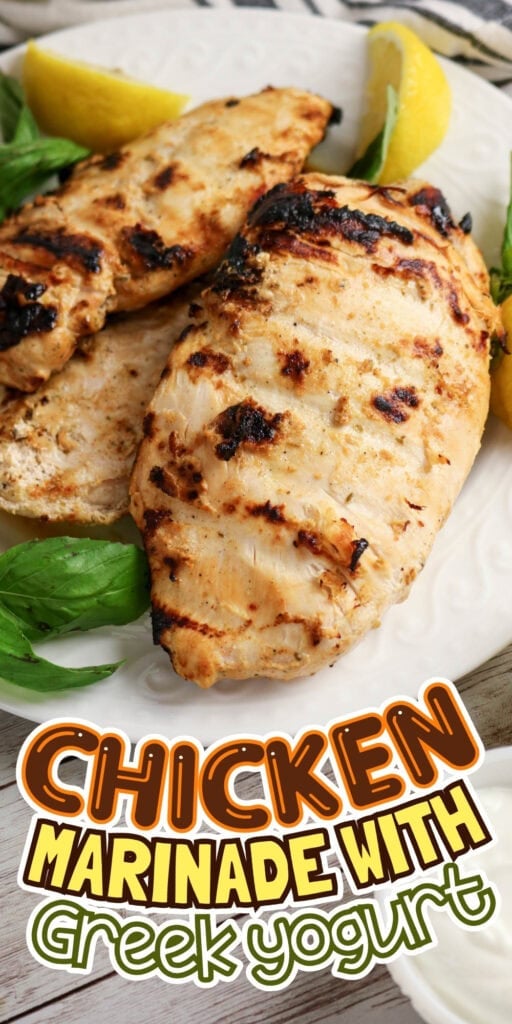 Grilled chicken breasts on a plate with lemon wedges and basil leaves.