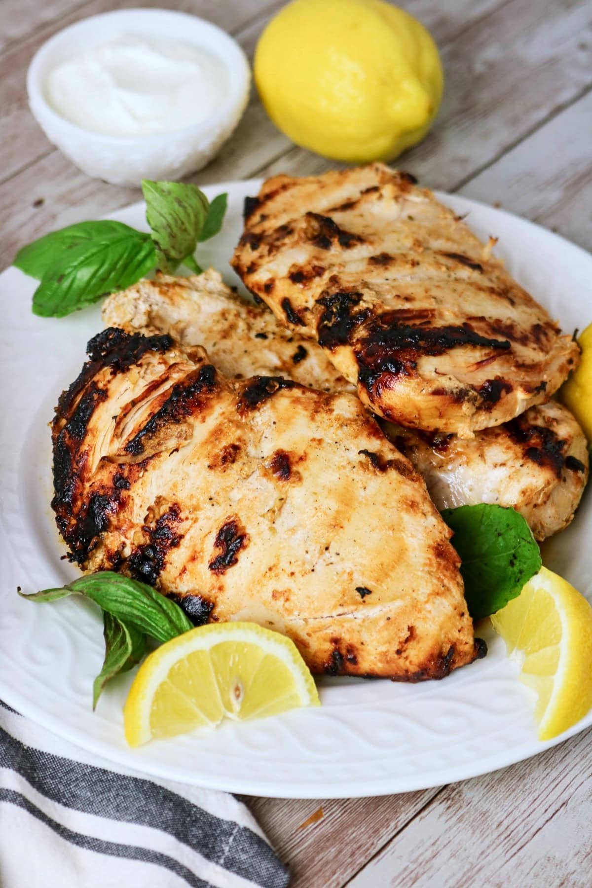 Grilled chicken breasts on a plate with lemon wedges and fresh basil.