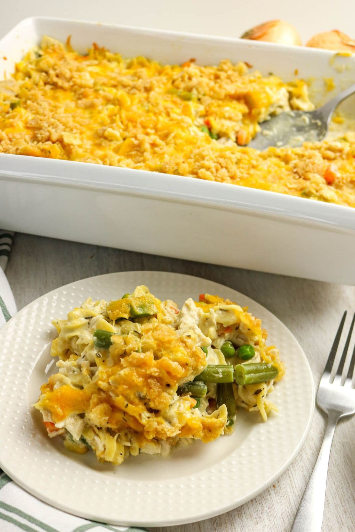 A serving of cheesy chicken casserole with vegetables beside a baking dish.
