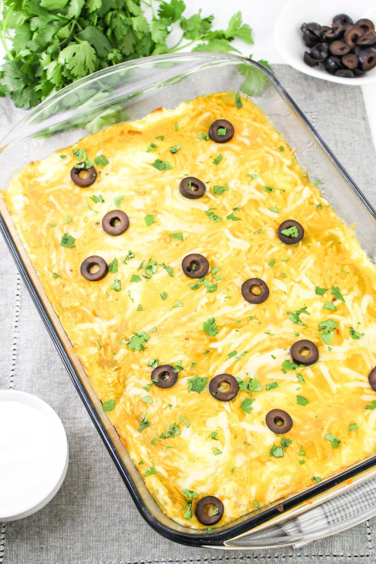 A baked casserole topped with cheese, sliced black olives, and chopped cilantro.