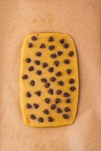 A rectangle of cookie dough with chocolate chips on parchment paper.