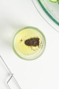 Small glass jar with yellow liquid and ground black pepper on top, shot from above.