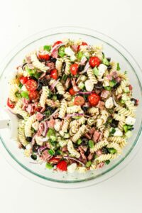 A bowl of pasta salad with rotini, tomatoes, olives, cheese, and herbs.