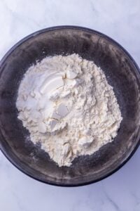 A black bowl with flour and solid shortening on a white marble surface.