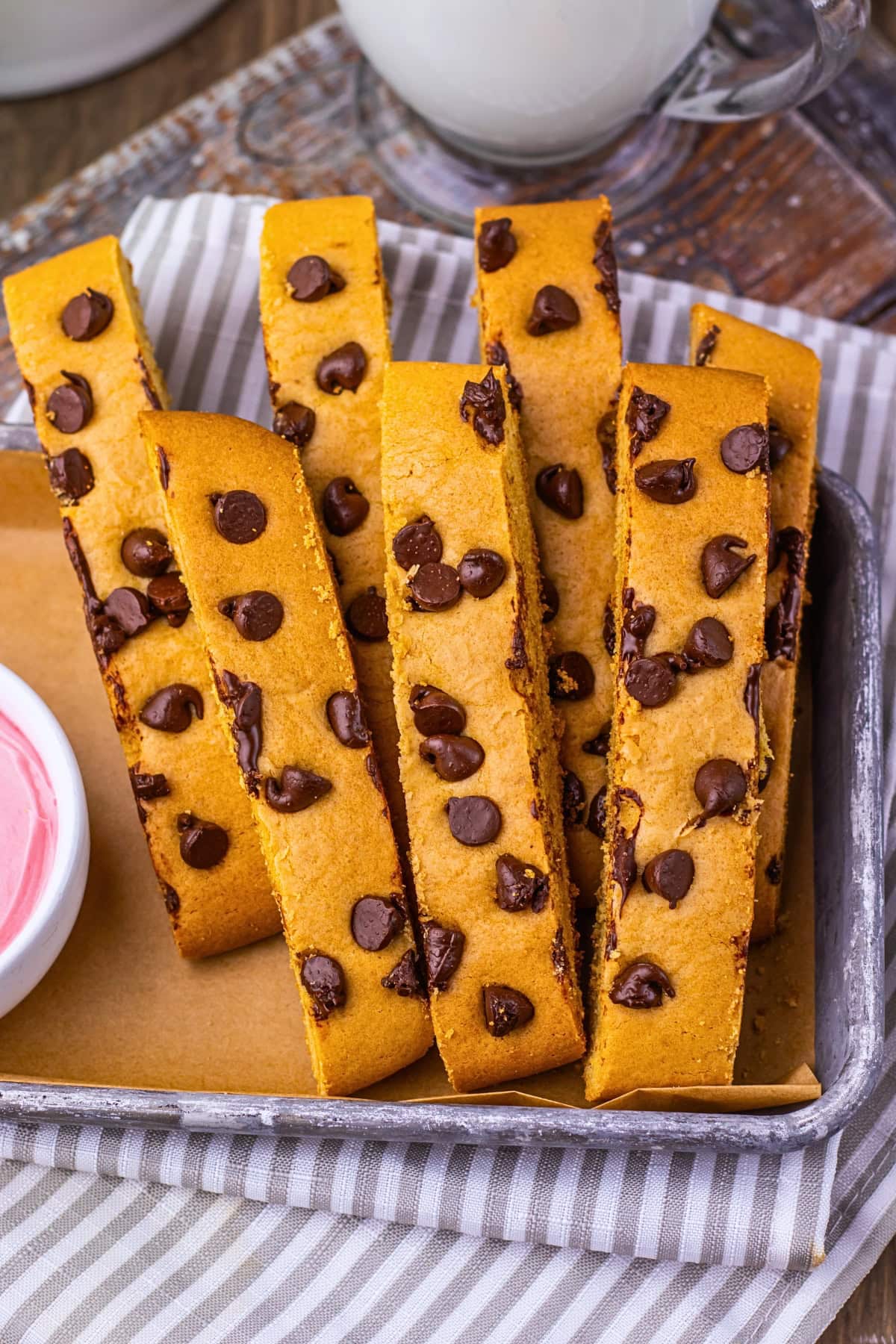 Five chocolate chip biscotti on a tray with a dish of pink dip beside them.