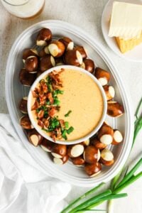 Bowl of cheese dip with bacon and chives, surrounded by pretzel bites.