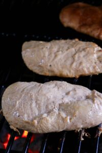 Two pieces of seasoned chicken breast grilling over an open flame.