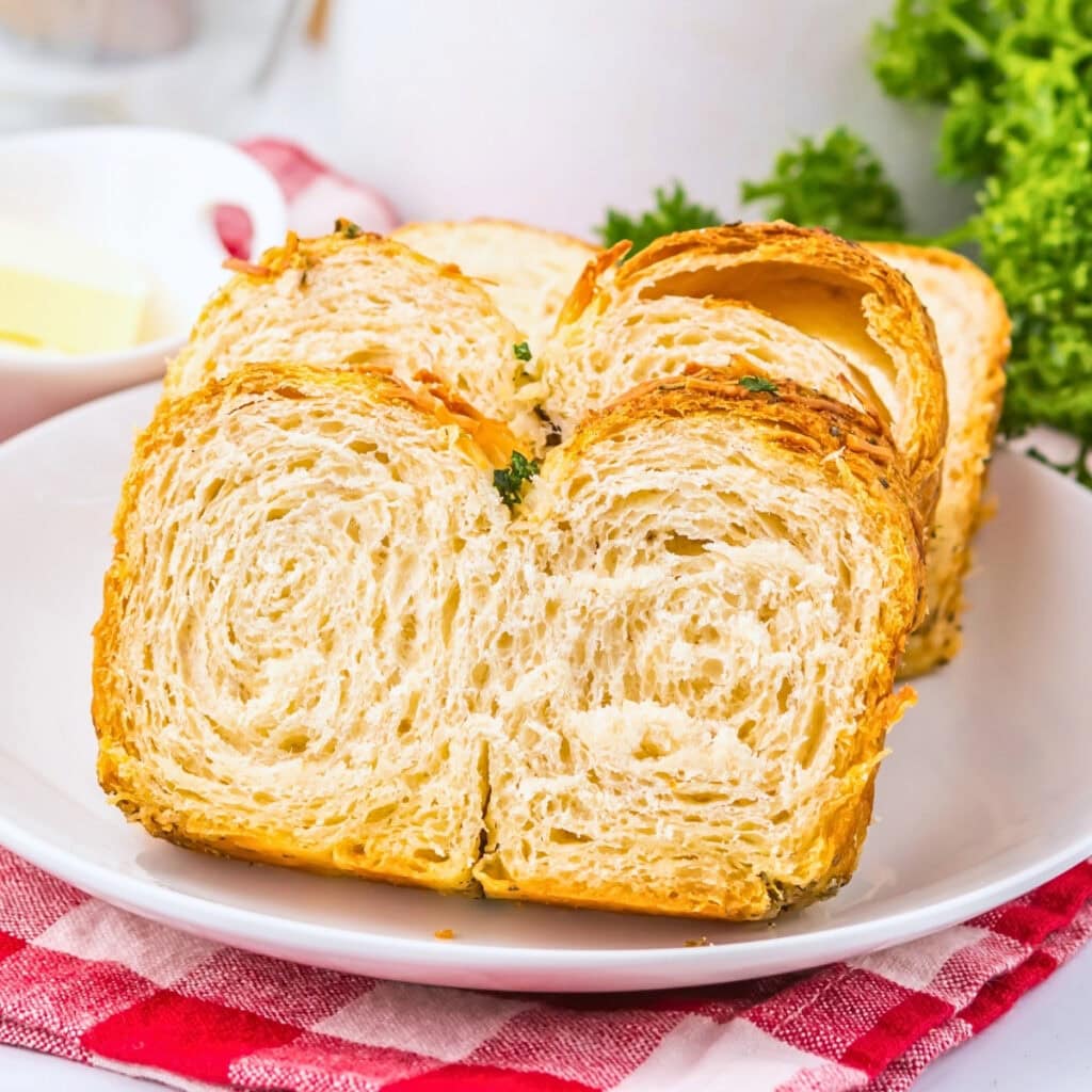 Sliced croissant bread on a white plate with parsley and a red checkered cloth.