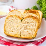 Sliced croissant bread on a white plate with parsley and a red checkered cloth.