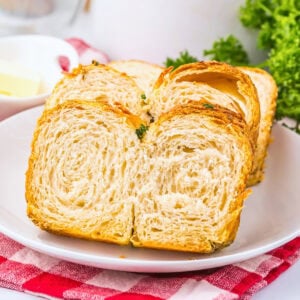 Sliced croissant bread on a white plate with parsley and a red checkered cloth.