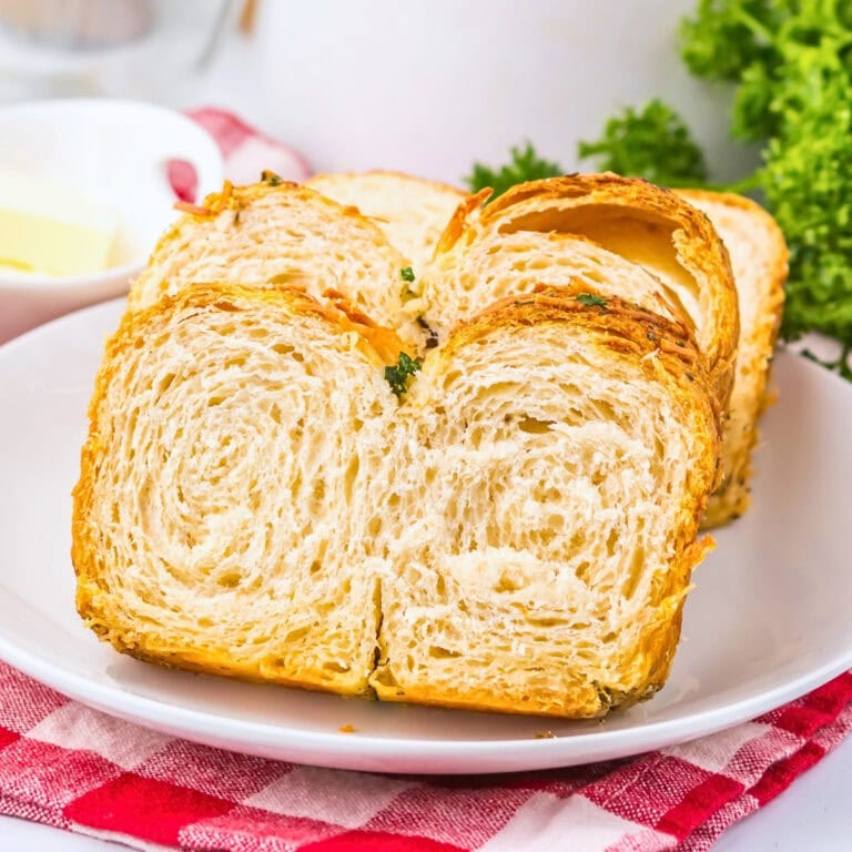 Sliced croissant bread on a white plate with parsley and a red checkered cloth.