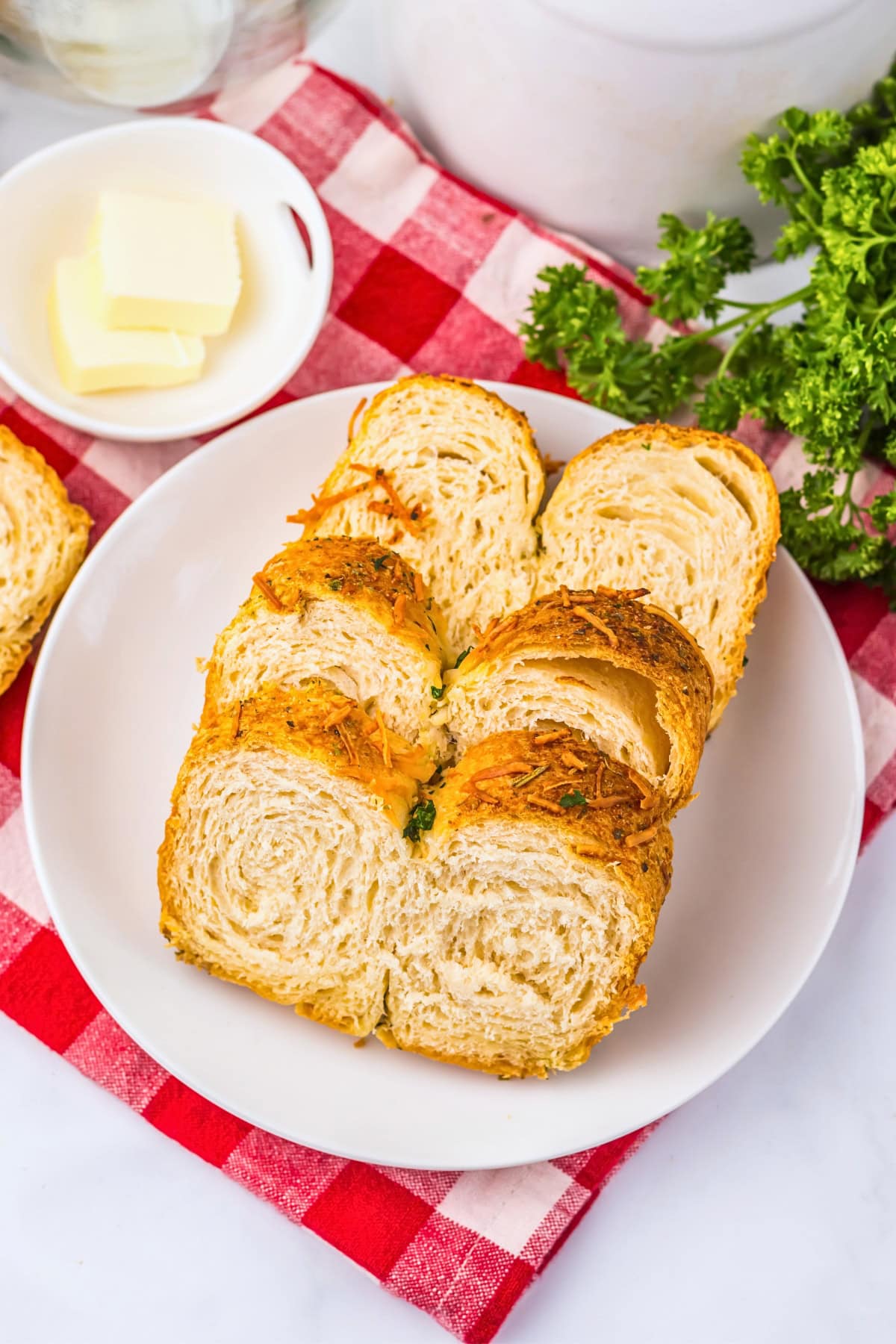 Two slices of bread on a white plate with butter on a red checkered cloth.