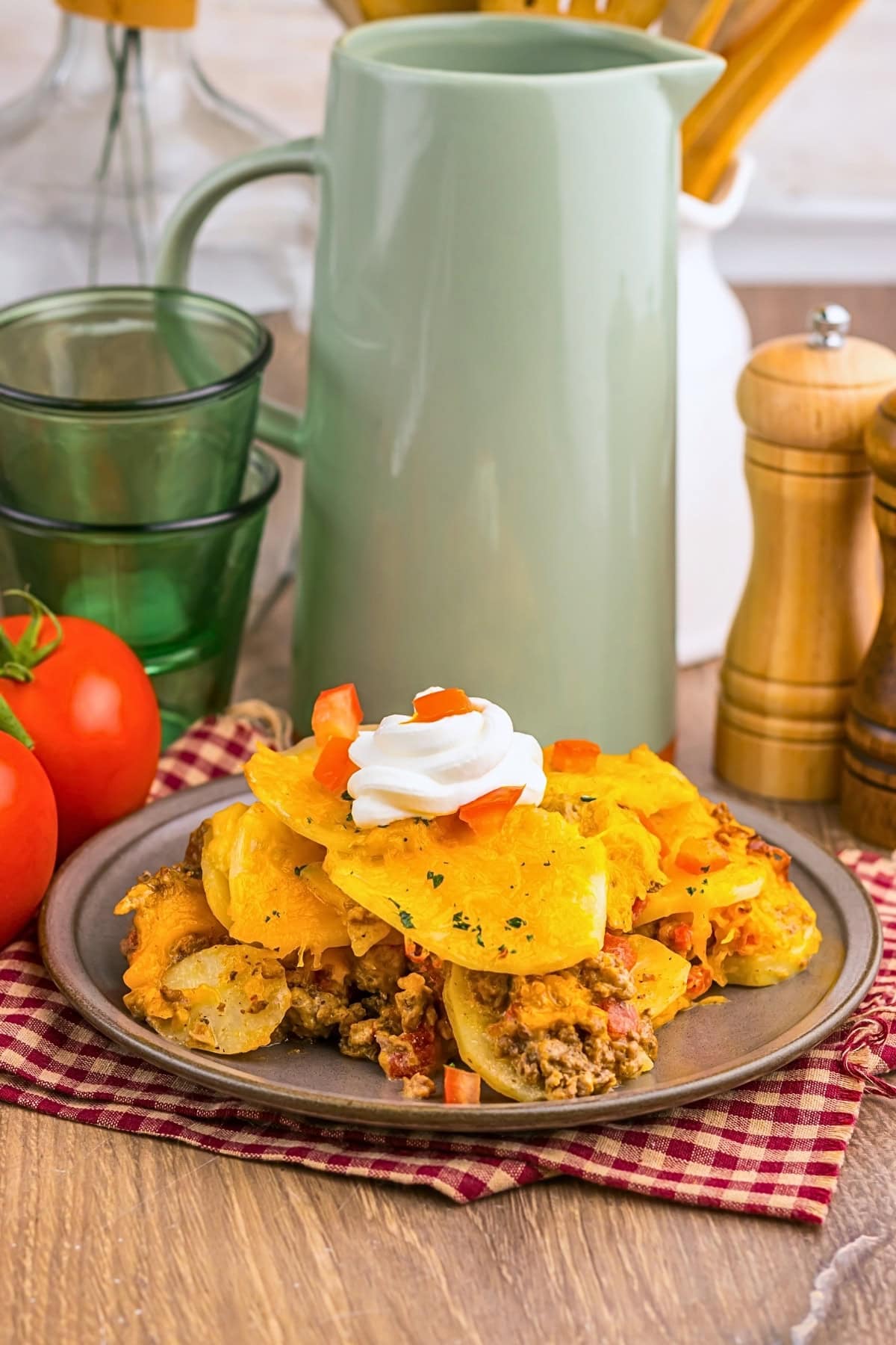 A plate of cheesy potato casserole topped with sour cream and diced tomatoes.