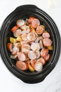 Sliced sausage and potatoes in a slow cooker, topped with seasoning.