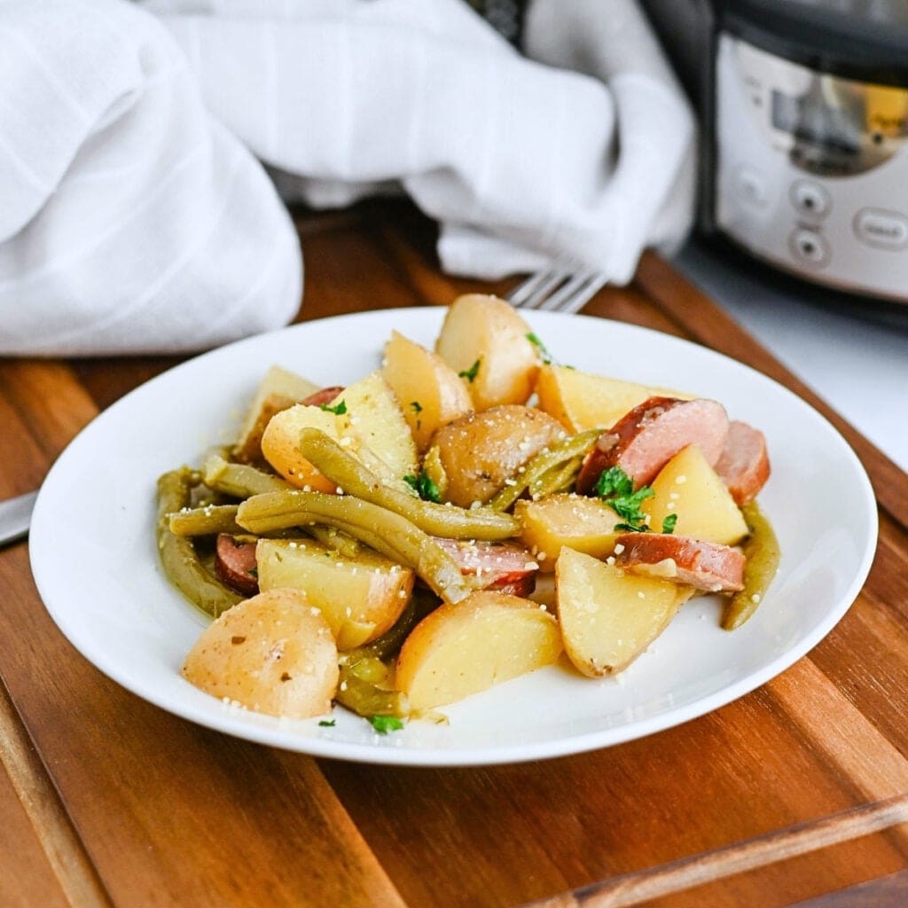 A plate of potatoes, green beans, and sausage on a wooden table.