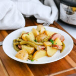A plate of potatoes, green beans, and sausage on a wooden table.
