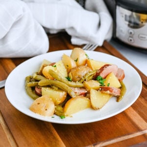 A plate of potatoes, green beans, and sausage on a wooden table.