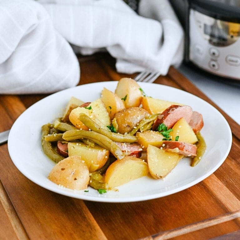 A plate of potatoes, green beans, and sausage on a wooden table.