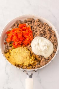 A skillet with cooked ground beef, diced tomatoes, sour cream, and seasoning.