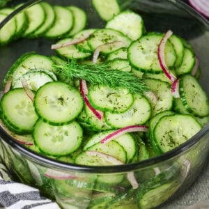 Glass bowl of cucumber salad with red onion, dill, and vinaigrette dressing.