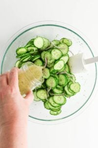 Sliced cucumbers and onions in a bowl, with dressing being poured on top.