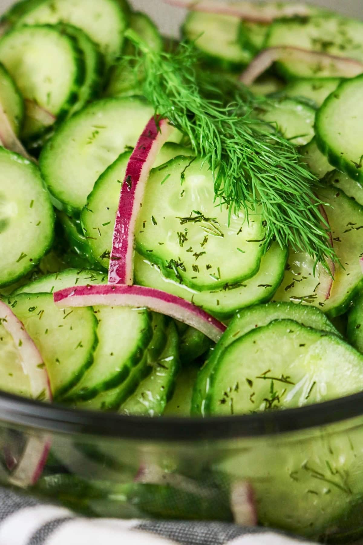 Sliced cucumber salad with red onions and dill in a glass bowl.