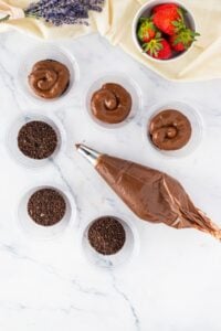 Chocolate mousse in cups, Oreo crumbs, piping bag, strawberries, and lavender on marble.