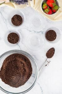 Glass bowls with crushed chocolate cookies, strawberries, and a metal spoon on marble.
