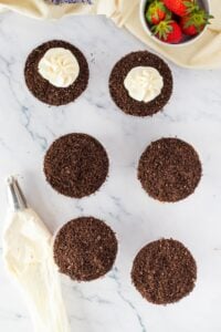 Six dessert cups with chocolate crumb topping, two with piped frosting on top.