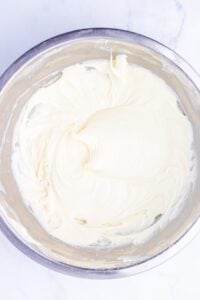 A metal bowl filled with creamy, whipped white frosting on a marble surface.