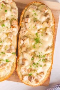 Two slices of bread topped with melted cheese, chicken pieces, and chopped parsley.