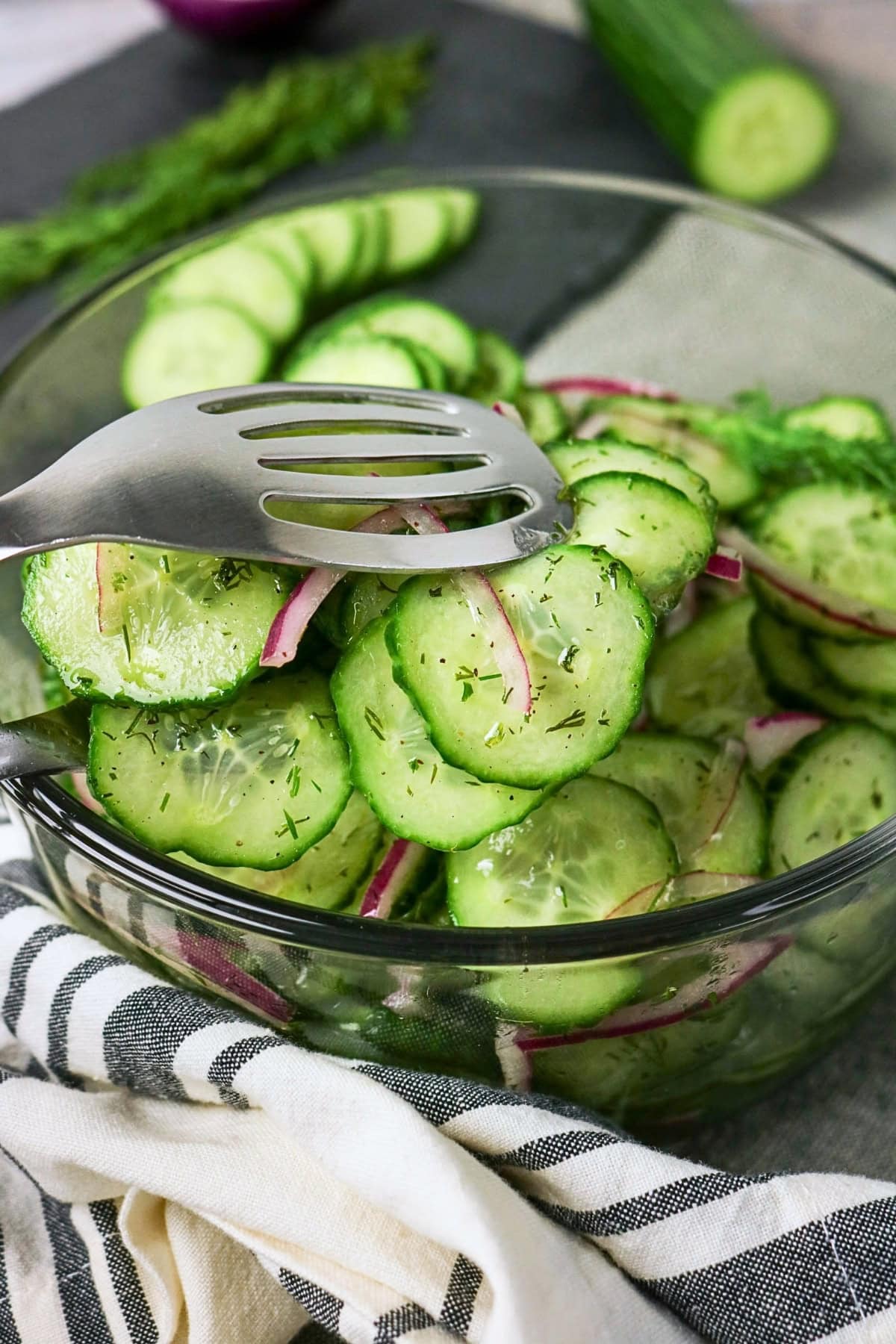 Sliced cucumber and red onion salad in a glass bowl with a serving spoon.