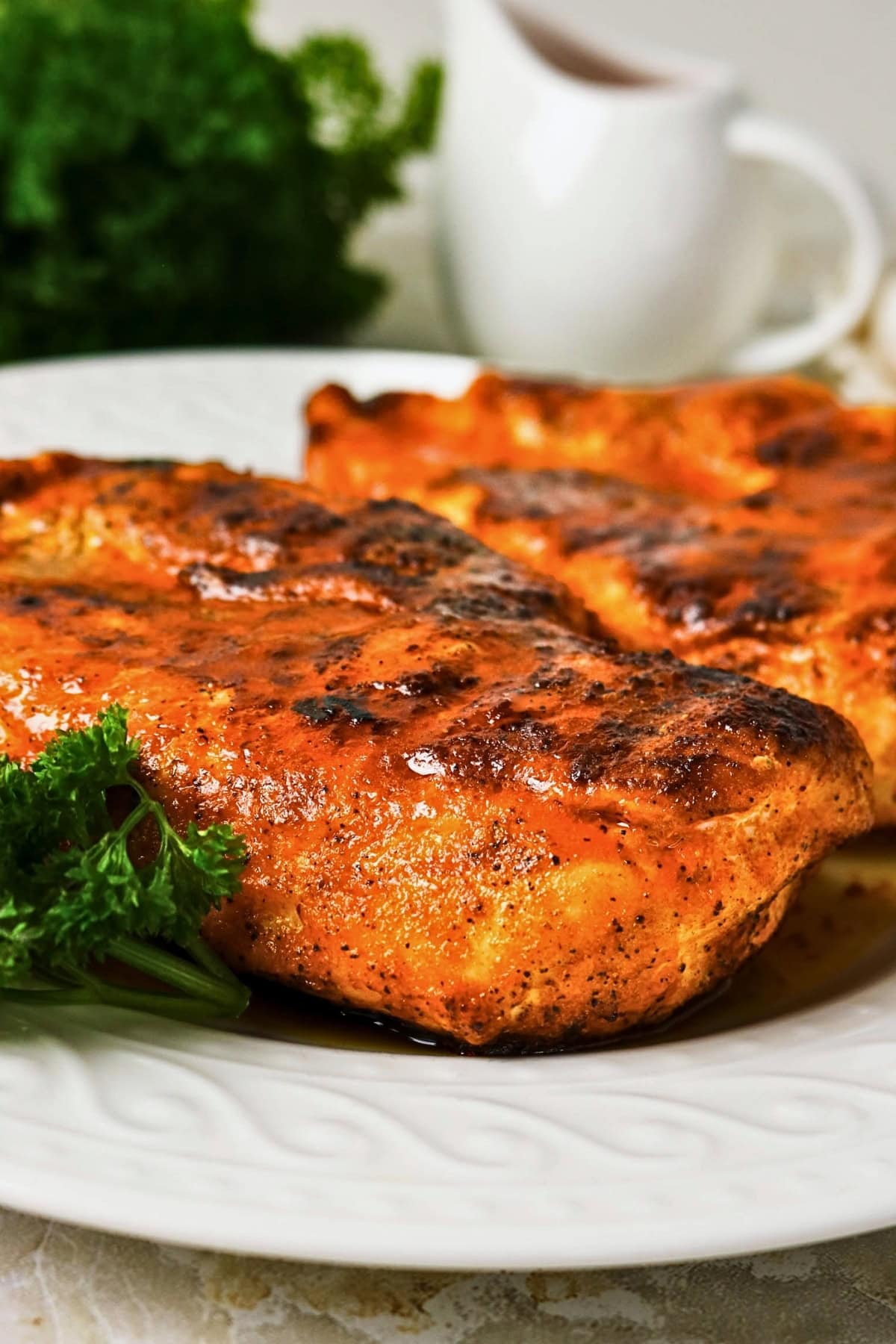 Grilled, seasoned chicken breasts on a plate with parsley garnish.