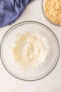 Cream cheese mixture whipped in a glass bowl, with crumbs in another bowl nearby.