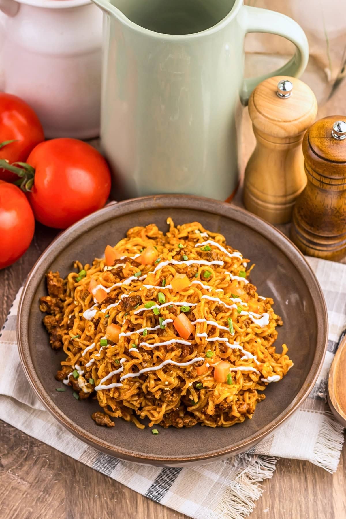 A plate of seasoned noodles with ground meat, diced tomatoes, and a creamy drizzle.