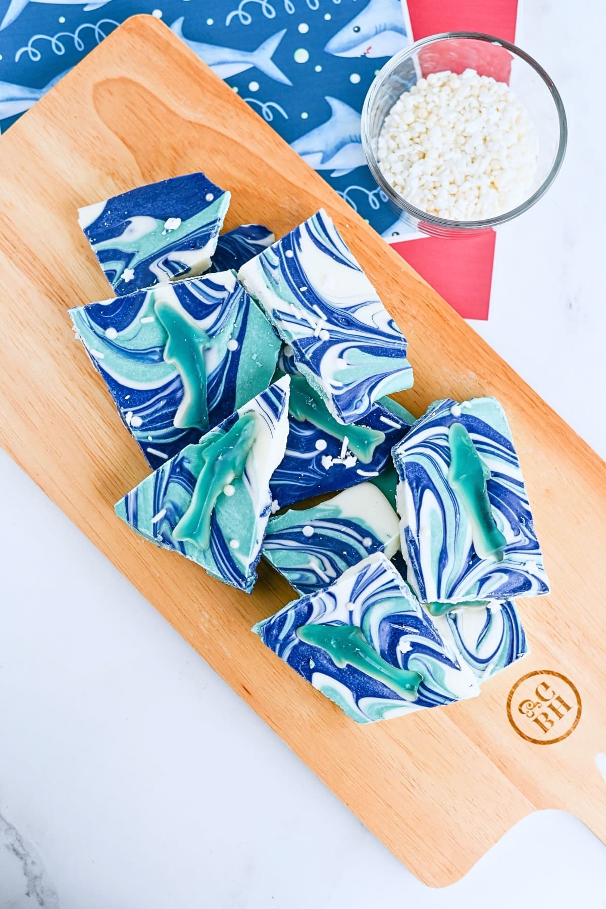 Blue and white marbled chocolate bark topped with gummy sharks on a wooden board.