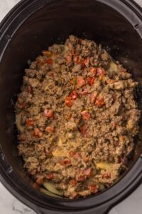 Ground beef with diced tomatoes cooking in a black slow cooker.