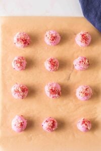 Twelve pink-coated cake balls with sprinkles on parchment paper.