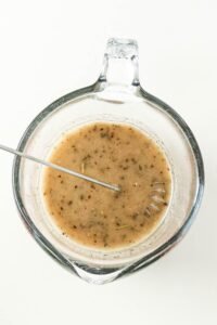 A glass measuring cup with mixed seasoning and a metal whisk inside.