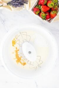 Mixing bowl with beaters, cream, powdered sugar, and orange zest; strawberries nearby.