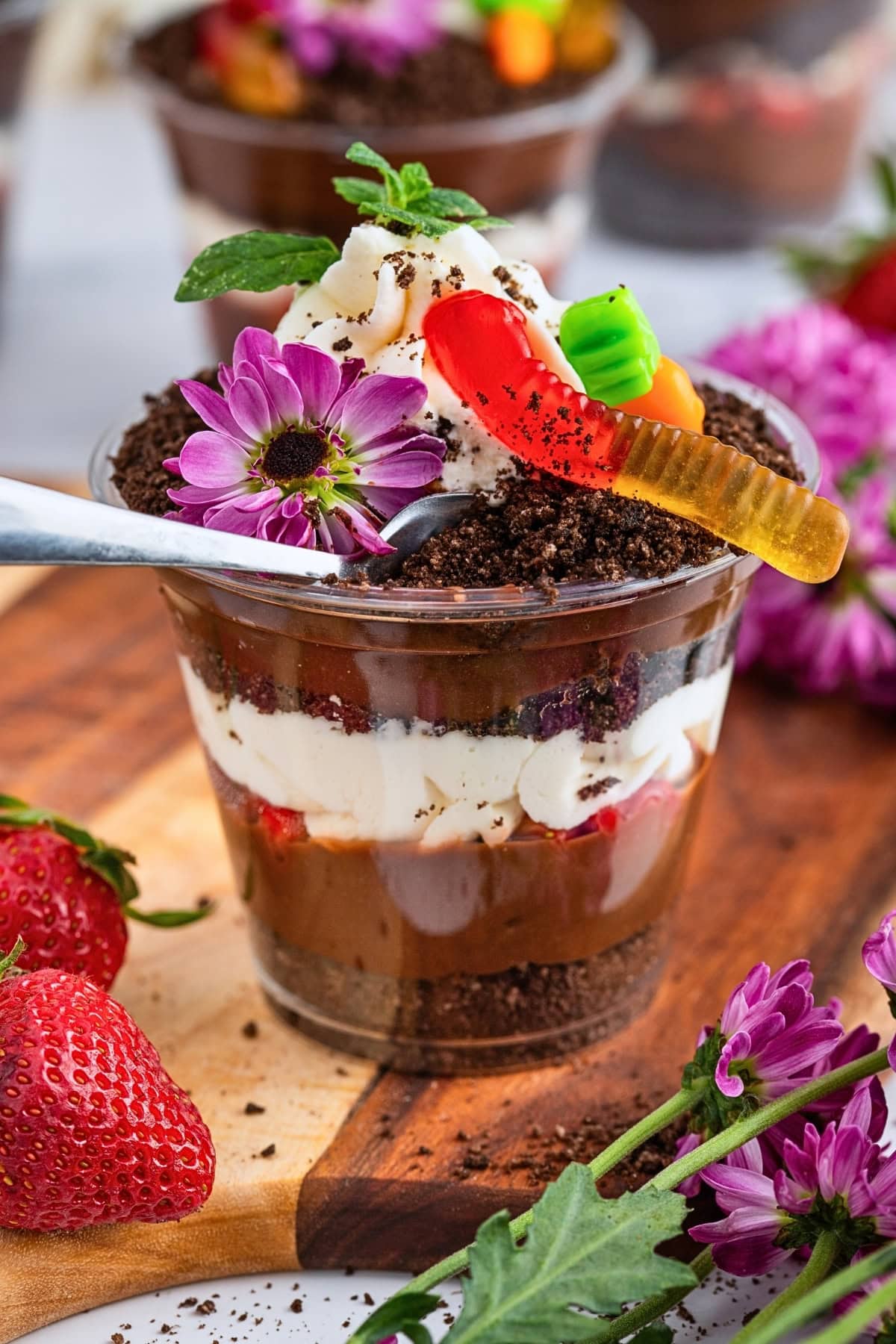 A chocolate pudding cup topped with whipped cream, gummy worms, and flowers.