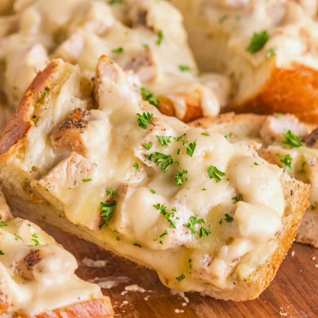 Toasted bread topped with melted cheese, chicken pieces, and chopped parsley.