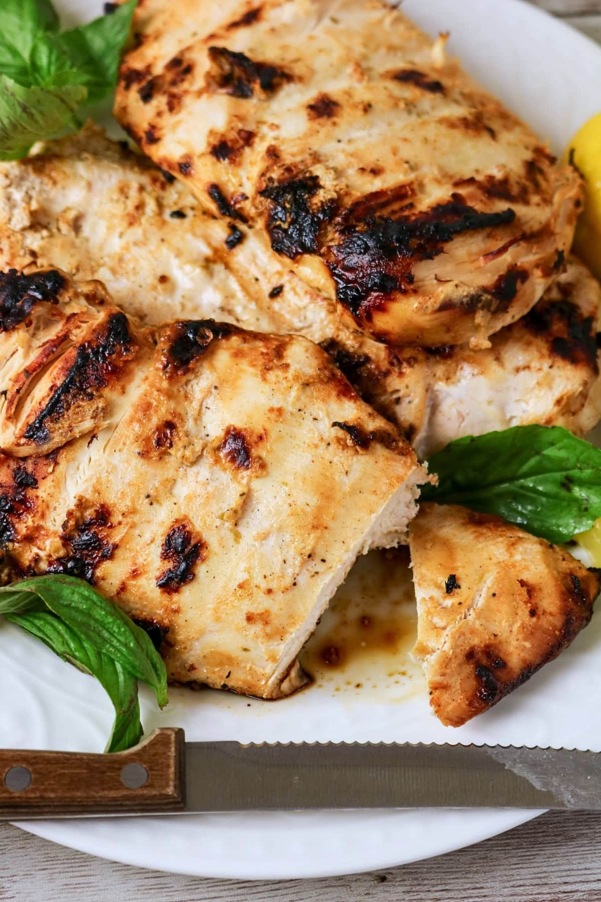 Grilled chicken breasts on a plate with basil leaves and a knife nearby.