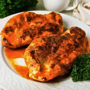 Two grilled chicken breasts with orange sauce, garnished with parsley on a plate.