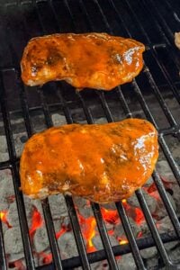 Two pieces of barbecue chicken with sauce grilling over hot coals on a grill.