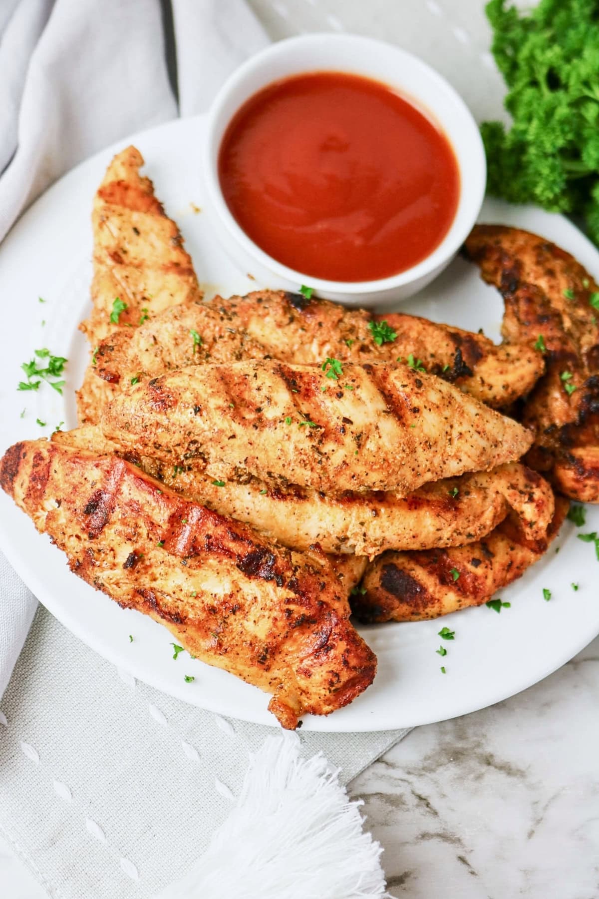 Grilled chicken tenders on a plate with a bowl of red dipping sauce.
