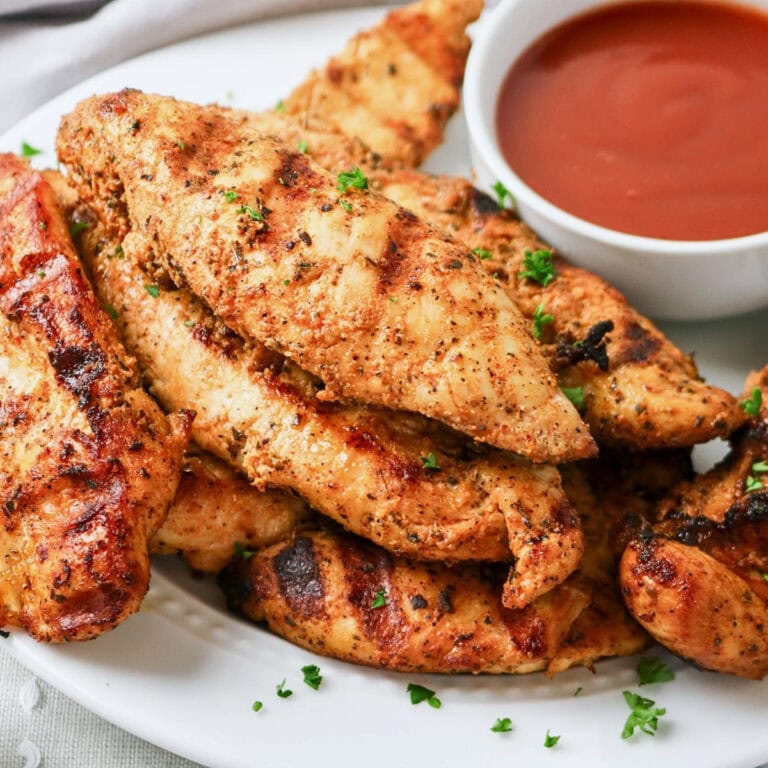Grilled chicken tenders on a plate with a bowl of dipping sauce.