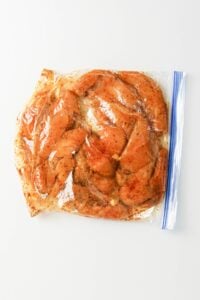 Raw marinated chicken pieces in a sealed plastic zipper bag on a white surface.