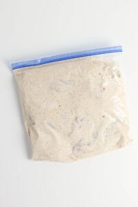 A sealed plastic bag filled with a creamy, seasoned marinade on a white surface.